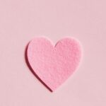 A simple pink felt heart on a light pink background, perfect for Valentine's Day themes.