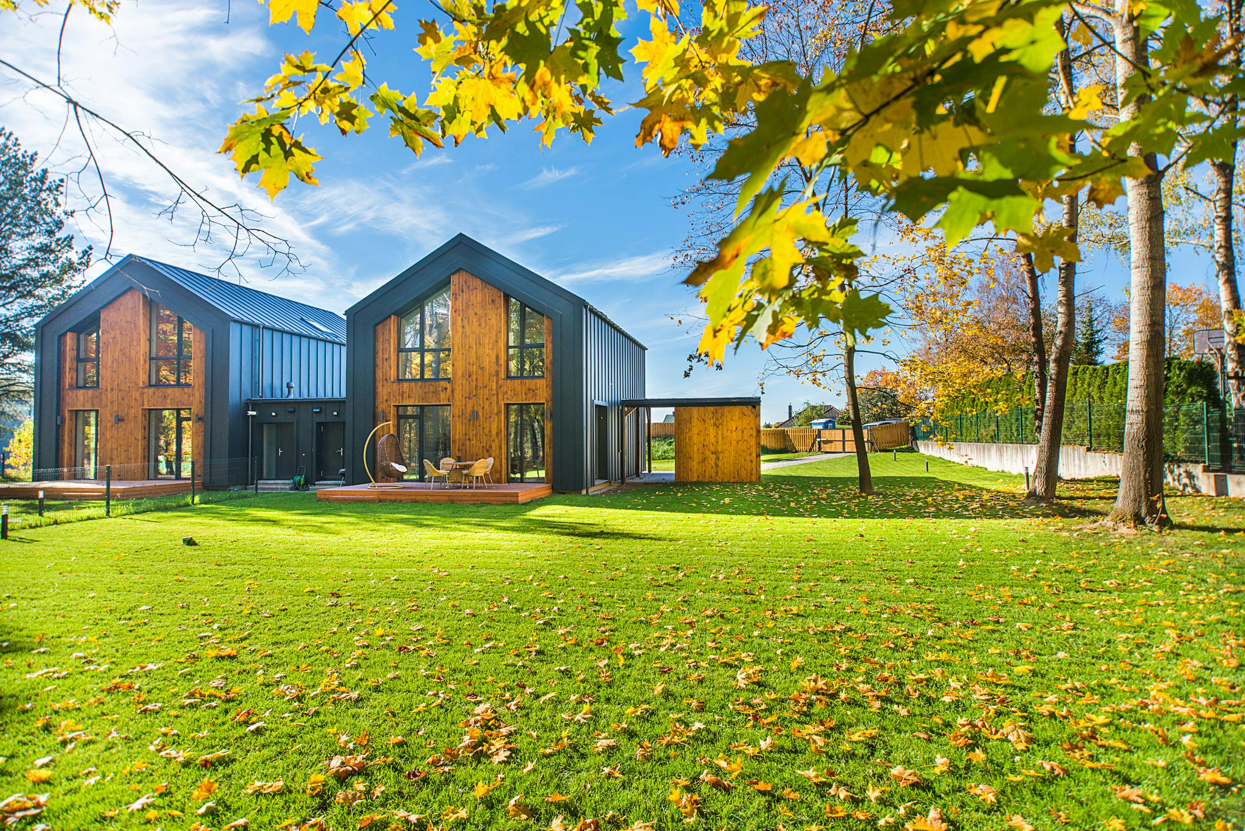 Contemporary wooden houses with lush green lawns surrounded by vibrant autumn foliage.